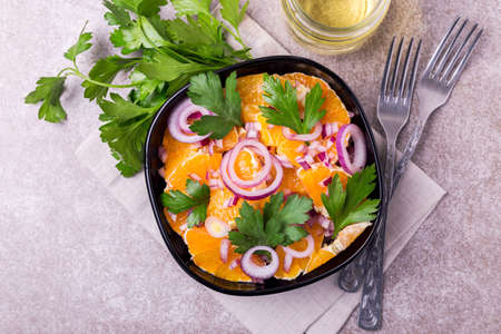 Traditional Italian Sicilian cuisine. Healthy orange salad with red onion, parsley and vinegar in black bowl on gray slate background. Copyspace, top view.の写真素材
