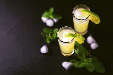 Tradtitional Italian homemade lemon and lime liqueur limoncello with ice and mint on black slate background. Alcoholic beverage. Selective focus.の写真素材