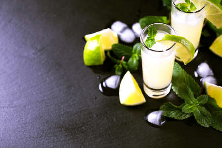 Tradtitional Italian homemade lemon and lime liqueur limoncello with ice and mint on black slate background. Alcoholic beverage. Selective focus.の写真素材