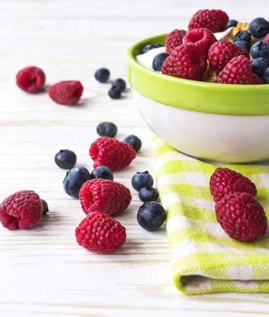 Bowl with cereals, raspberries, yogurt and blueberries. Healthy corn flakes breakfast on the white wooden table. Delicious meal.の写真素材