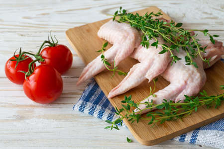 Raw chicken wings with fresh organic thyme, pepper and tomatoes on wooden table.の写真素材