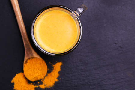 Traditional Indian cuisine. Turmeric milk with cinnamon, saffron, cardamom and turmeric on black slate background. Copyspace, top view, flatlayの写真素材