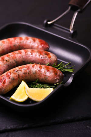 Summer food. Grilled homemade sausages with rosemary and lime on iron grill frying pan on black...
