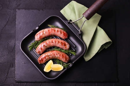 Summer food. Grilled homemade sausages with rosemary and lime on iron grill frying pan on black stone. Copyspace, top view, flat layの写真素材