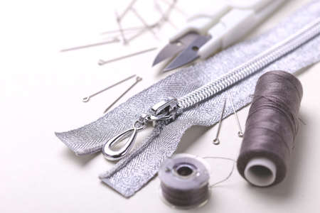 Silver sewing pins, scissors, zipper and plastic bobbin with colour threads on white studio backgroundの写真素材