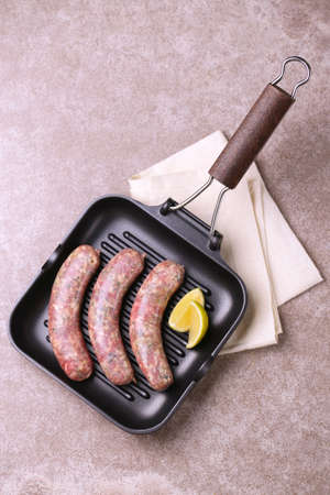 Summer food. Raw homemade sausages with rosemary and lime on iron grill frying pan on gray stone. Copyspace, top view, flat layの写真素材