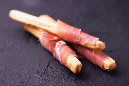 Traditional italian bread sticks grissini with prosciutto ham on a plate, horizontal viewの写真素材