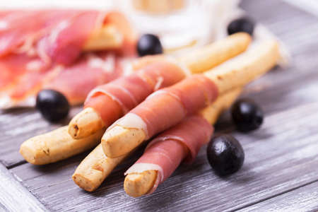 Traditional italian bread sticks grissini with prosciutto ham on a plate, horizontal view