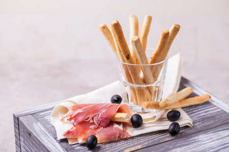 Traditional italian bread sticks grissini with prosciutto ham on a plate, horizontal viewの写真素材