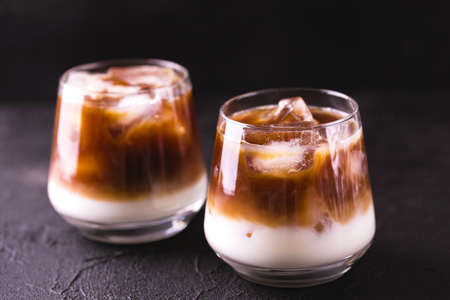 Iced coffee in glasses with milk and cream. Black background. Horizontal view. Copy space