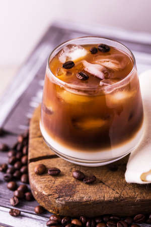 Iced coffee in glasses with milk and cream. White background, wooden table. Horizontal view. Copy...