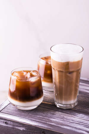 Iced coffee in glasses with milk and cream. White background, wooden table. Horizontal view. Copy...