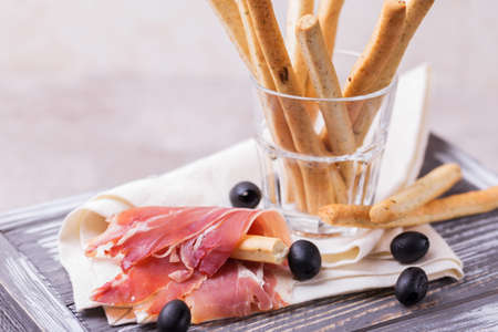 Traditional italian bread sticks grissini with prosciutto ham on a plate, horizontal viewの写真素材