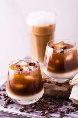 Iced coffee in glasses with milk and cream. White background, wooden table. Horizontal view. Copy...