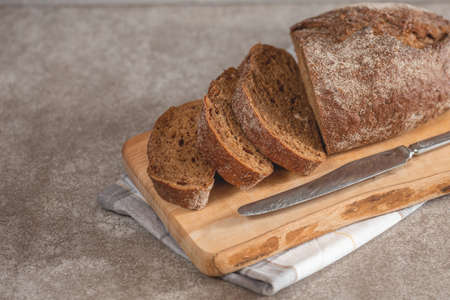 Fresh sliced loaf of rye bread on the wooden cutting board background with napkin and knife....