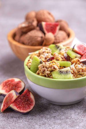 Bowl of homemade granola with fresh bananas and figs on grey slate background.  Horizontal view....