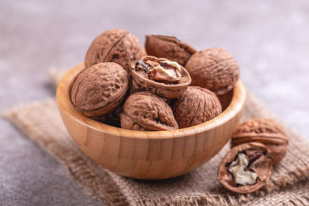 Whole walnuts in wooden bowl. Harvest concept. Grey slate background. Horizontal view. Copy space