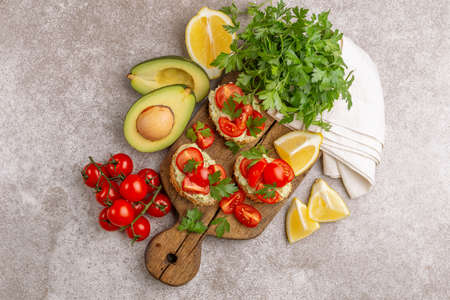 Bruschetta with chopped cherry tomatoes, puree avocado and fresh parsley on the wooden cutting board.の写真素材