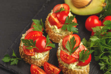 Bruschetta with chopped cherry tomatoes, puree avocado and fresh parsley on the black slate backgroundの写真素材