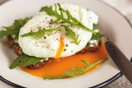 Rye bread toast with poached egg, dairy cream, spices and arugula and cup of coffee on the gray...