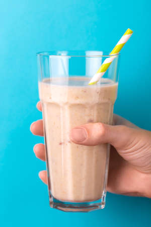 Fresh banana and almond smoothie in tumbler with paper straw on bright blue background. Horizontal view. Copy spaceの写真素材