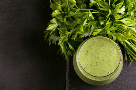 Fresh spinach and avocado smoothie in glass with parsley on black slate background. Top view. Copy spaceの写真素材