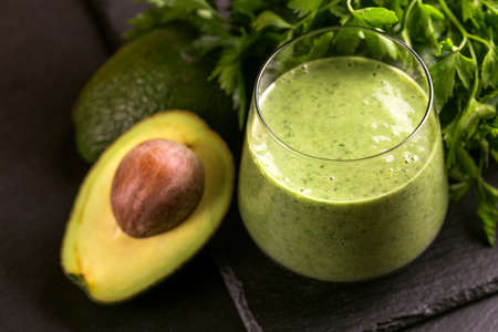 Fresh spinach and avocado smoothie in glass with parsley on black slate background. Horizontal view. Copy spaceの写真素材