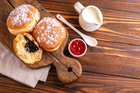 Tasty sweet sugary chocolate donuts with raspberry jam and milk on old wooden rustic cutting board. Traditional Jewish sweet Hanukkah dish. Wooden backgroundの写真素材