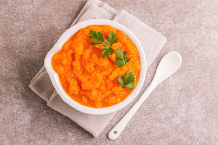 Bright tasty pureed carrot soup in clay bowl with napkin. Healthy food concept. Gray marble background. Horizontal view. Copy spaceの写真素材