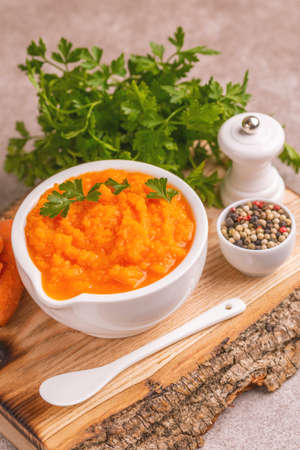 Bright tasty pureed carrot soup in clay bowl on woden cutting board. Healthy food concept. Gray marble background. Horizontal view. Copy spaceの写真素材