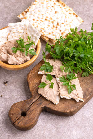 Pieces of matzah with homemade liver pate with parsley and onion on old wooden cutting board with burlap napkin. Gray marble background. Copy spaceの写真素材