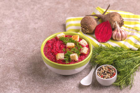 Bright tasty pureed beetroot soup in clay bowl with ingredients. Healthy food concept. Gray marble background. Horizontal view. Copy spaceの写真素材