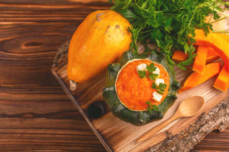 Bright tasty pureed pumpkin soup served in a hollowed pumpkin with ingredients. Healthy food concept. Rustic wooden background. Top view. Copy spaceの写真素材