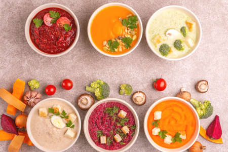 Variety of colorful tasty vegetables cream soups and fresh ingredients for soups. Healthy food concept or vegetarian food. Gray marble backgroundの写真素材