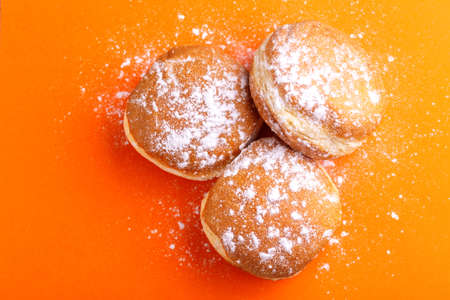 Tasty sweet donuts with powdered sugar on bright orange background. Traditional Jewish sweet Hanukkah dishの写真素材