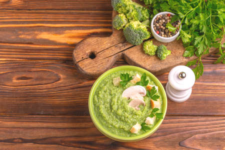 Fresh tasty pureed broccoli soup in clay bowl with ingredients on cutting board. Healthy food concept. Rustic wooden background. Top view. Copy spaceの写真素材