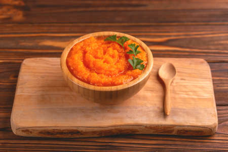Bright tasty pureed carrot soup in wooden bowl on cutting board. Healthy food concept. Rustic wooden background. Horizontal view. Copy spaceの写真素材