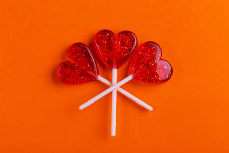 Three red sweet tasty lollipops in shape of heart on bright orange background. St. Valentine's day. Copy spaceの写真素材