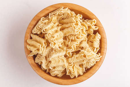 Uncooked instant noodles in wooden bowl on white marble background. Copy space.の写真素材