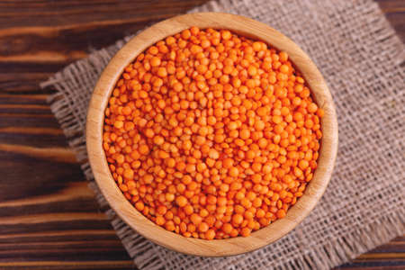 Raw red lentils in wooden bowl with burlap napkin on rustic wooden backgroundの写真素材