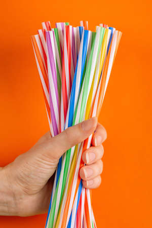 Woman is holding colorful plastic straws in hand on bright background. Event and party supplies. Earth pollution conceptの写真素材