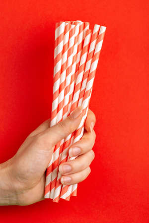 Woman is holding red and white paper straws in hand on bright background. Event and party supplies. Earth pollution concept. Copy spaceの写真素材