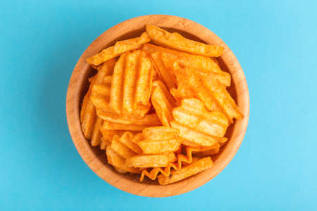 Crispy corrugated potato chips in wooden bowl on bright blue background. Junk food. Copy spaceの写真素材