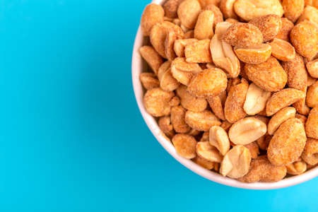 Roasted peanuts in paper cup on bright blue background. Movie snacks. Copy spaceの写真素材