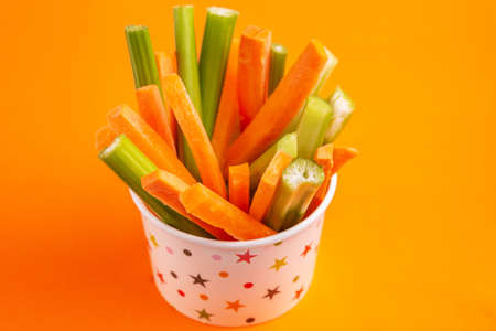 Fresh carrots and celery sticks in paper cup on bright colorful background. Healthy food concept. Copy spaceの写真素材