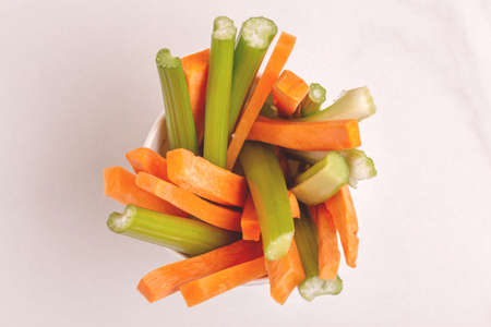 Fresh carrots and celery sticks in paper cup on light marble background. Healthy food concept. Copy space. Top viewの写真素材