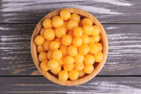 Cheese puff balls in wooden bowl on wooden background. Cinema snacks. Copy spaceの写真素材