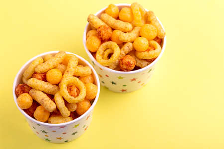 Assorted puff corn snacks in two paper cup on bright colored background. Snacks for watching movies. Copy spaceの写真素材