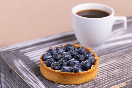 Tasty blueberry tartlet with vanilla cream and cup of coffee on rustic wooden background. Copy space. Horizontal view