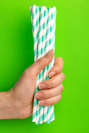Woman is holding green and white paper straws in hand on bright background. Event and party supplies. Earth pollution concept. Copy spaceの写真素材